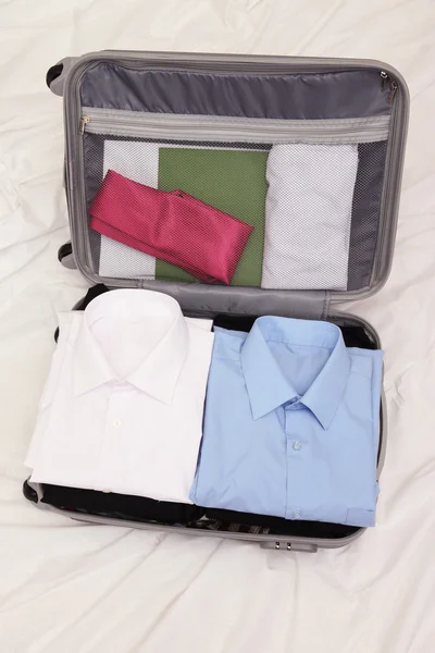 Otevřít šedý kufr s oblečením na posteli — Stock fotografie