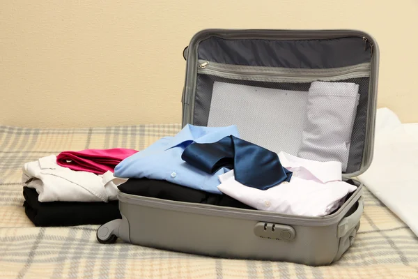 Open grey suitcase with clothing on bed — Stock Photo, Image