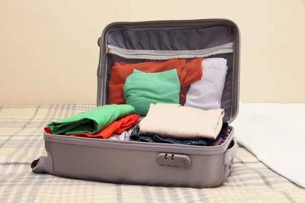 Открытый серый чемодан с одеждой на кровати — стоковое фото