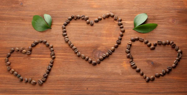 Kávová zrna s listy na dřevěné pozadí — Stock fotografie