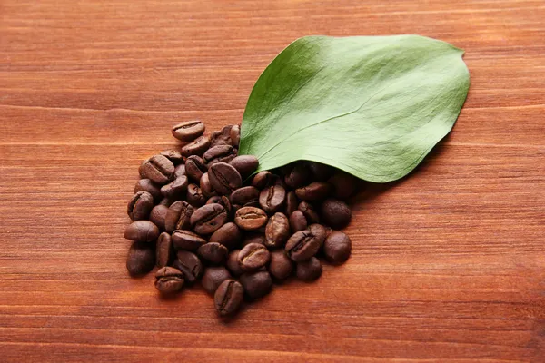 Coffee beans with leaves on wooden background — Stock Photo, Image
