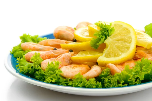 Вареные креветки с лимоном и листьями салата на тарелке, изолированные на белом — стоковое фото