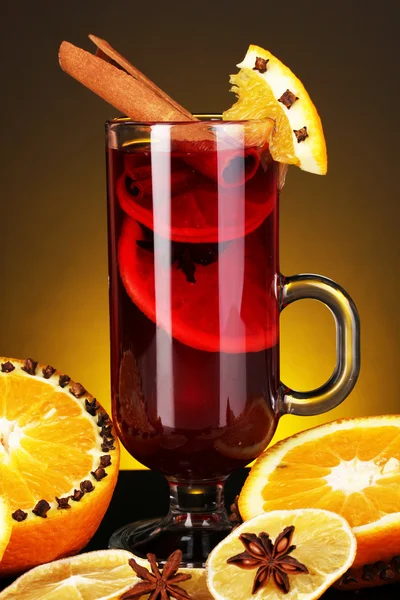 Fragrant mulled wine in glass with spices and oranges around on yellow background — Stock Photo, Image