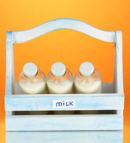 Milk in bottles in wooden box on orange background — Stock Photo, Image