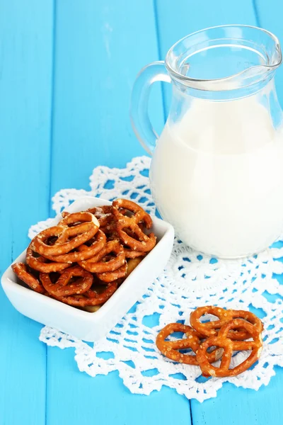Sabrosos pretzels en tazón blanco y jarra de leche en la mesa de madera de cerca — Foto de Stock