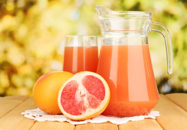 Full glass and jug of grapefruit juice and grapefruits on wooden table outdoor — Stock Photo, Image