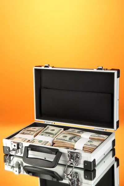 Maleta con billetes de 100 dólares sobre fondo naranja — Foto de Stock