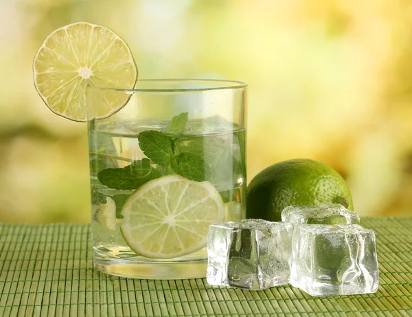 Glass of water with ice, mint and lime on table on bright background — Stock Photo, Image