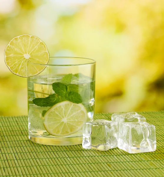 Glass of water with ice, mint and lime on table on bright background — Stock Photo, Image