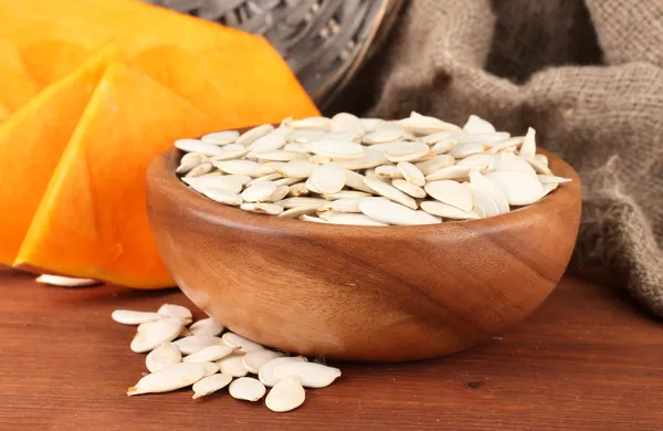 Pumpkin seeds in wooden bowl, on sackcloth background — Stock Photo, Image
