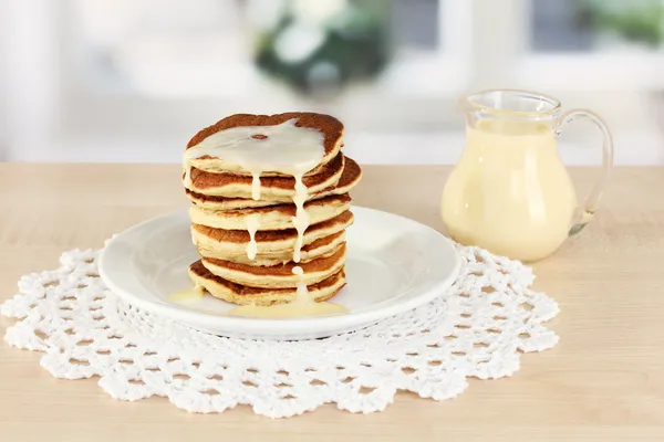 Zoete pannenkoeken op plaat met gecondenseerde melk op tafel in de keuken — Stockfoto