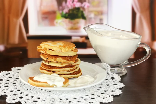 Sweet pancakes on plate with sour cream on table in room — Stock Photo, Image