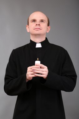 Genç papaz holding mum gri arka plan üzerinde elinde portresi