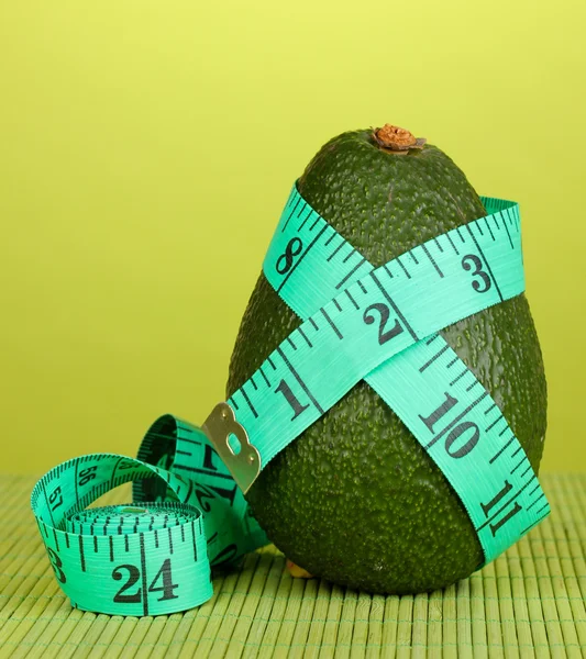 Avocado con nastro di misurazione su sfondo verde — Foto Stock