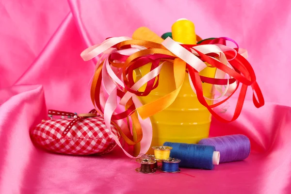 Barevný kbelík s mnohobarevnou stuhy a podprocesu na pozadí růžové látky — Stock fotografie