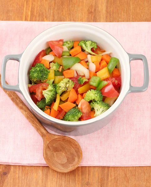 Рагу из овощей в сером горшке на цветной салфетке на деревянном фоне — стоковое фото