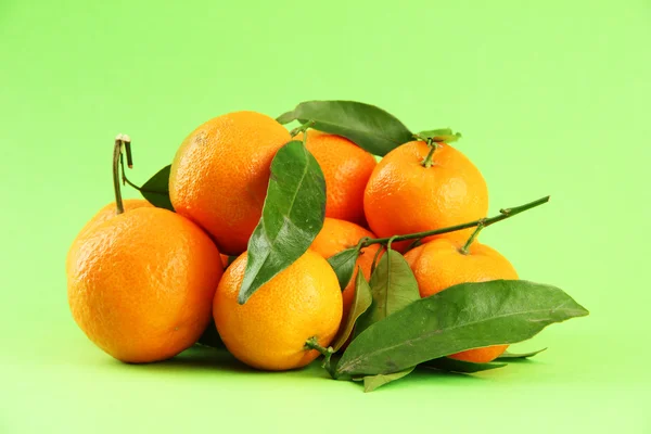 Ripe sweet tangerines with leaves, on green background — Stock Photo, Image