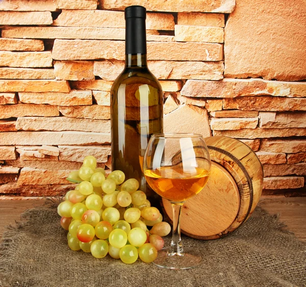 Композиция вина, деревянной бочки и винограда на столе на фоне кирпичной стены — стоковое фото