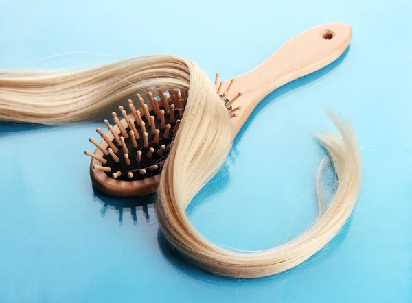 Wooden comb brush with hair, on blue background — Stock Photo, Image