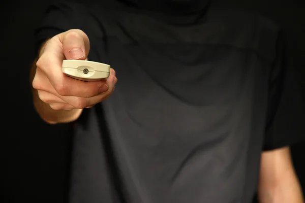 Mão de homem segurando um controle remoto de TV, no fundo escuro — Fotografia de Stock