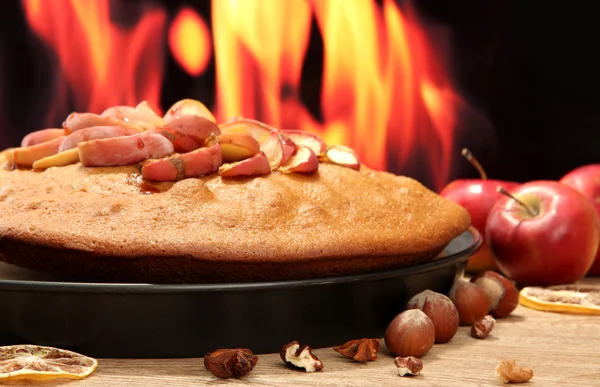 Tasty homemade pie with apples and nuts, on wooden table on flame background — Stock Photo, Image