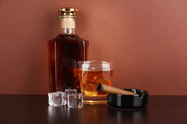 Μπουκάλι και ποτήρι ουίσκι και πούρα σε καφέ φόντο — Φωτογραφία Αρχείου