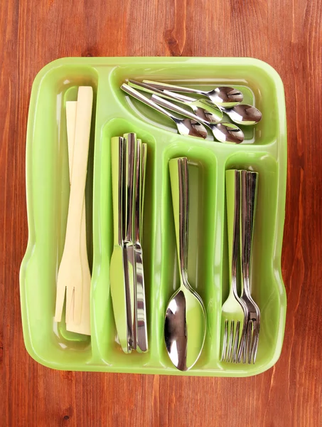 Green plastic cutlery tray with checked cutlery on wooden table — Stock Photo, Image