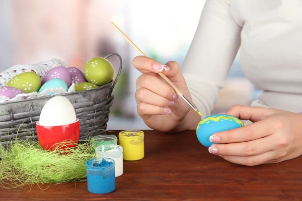 Mujer joven pintando huevos de Pascua, sobre fondo brillante —  Fotos de Stock