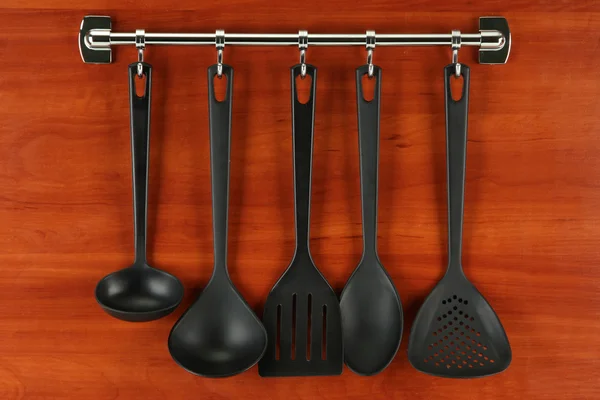 Black kitchen utensils on silver hooks, on wooden background — Stock Photo, Image