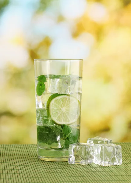 Bicchiere d'acqua con ghiaccio, menta e calce sul tavolo su sfondo luminoso — Foto Stock
