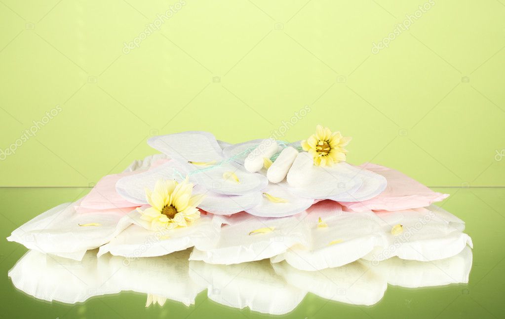 various types of sanitary pads and tampons on green background close-up