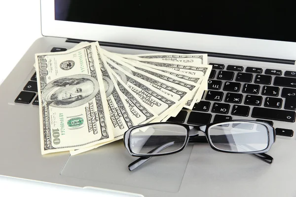 Деньги в очках на ноутбуке крупным планом — стоковое фото