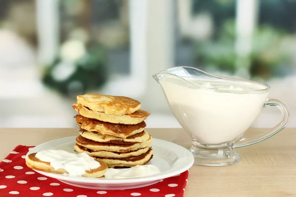 Sweet pancakes on plate with sour cream on table in kitchen — Stock Photo, Image