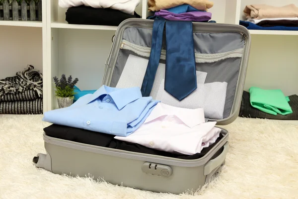 Open grey suitcase with clothing in room — Stock Photo, Image
