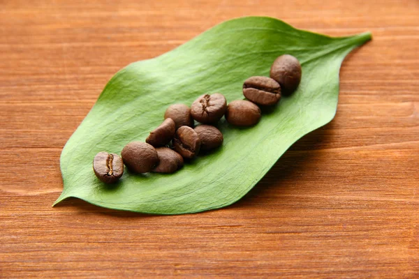 Kaffeebohnen mit Blättern auf Holzgrund — Stockfoto