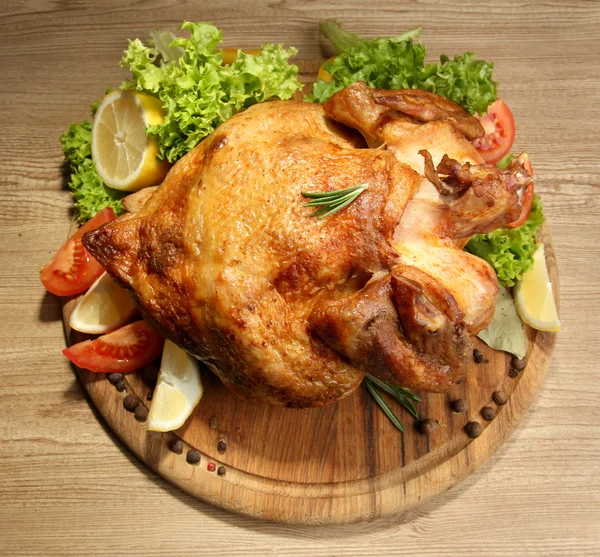 Poulet rôti entier avec légumes dans une assiette, sur une table en bois — Photo