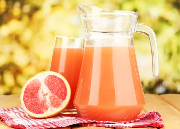 Vol glas en kruik van grapefruitsap en grapefruits op houten tafel buiten — Stockfoto