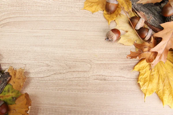 Bellotas marrones sobre hojas de otoño, sobre fondo de madera — Foto de Stock