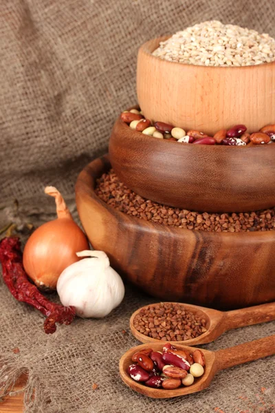 Grano crudo, grano saraceno e fagioli in ciotole di legno su tavola su fondo sacco — Foto Stock