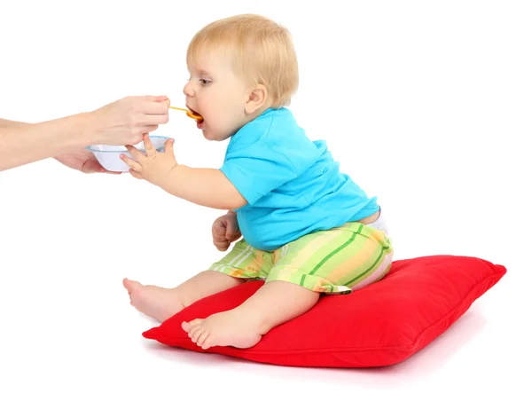 Niño sentado en la almohada roja y comiendo puré de manzana, aislado en blanco —  Fotos de Stock