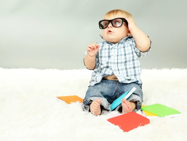 Маленький мальчик с разноцветными книгами, на белом ковре — стоковое фото