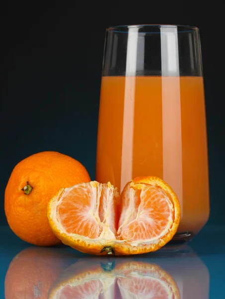 Delicious tangerine juice in glass and mandarins next to it on dark blue background — Stock Photo, Image