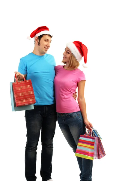 Mladý pár v santa klobouky nakupování a drží mnoho nákupní tašky izolované na bílém — Stock fotografie
