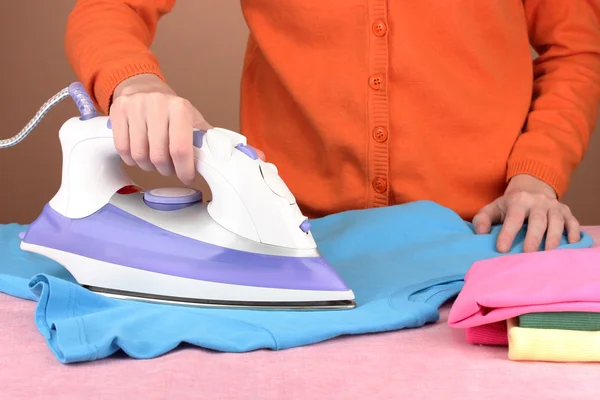 Young woman ironing her clothes, on brown background — Stock Photo, Image