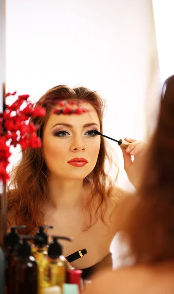 거울 근처에서 화장하는 젊고 아름다운 여성 — 스톡 사진