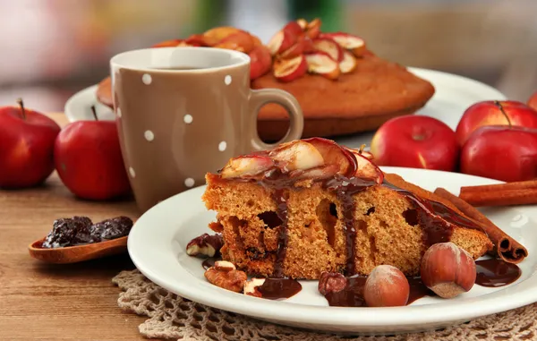 Fetta di gustosa torta fatta in casa con cioccolato e mele e tazza di caffè, su tavolo di legno — Foto Stock