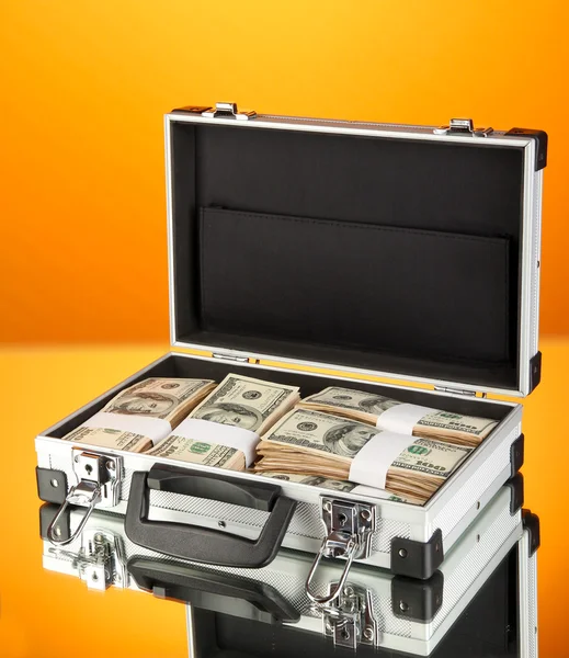 Maleta con billetes de 100 dólares sobre fondo naranja —  Fotos de Stock