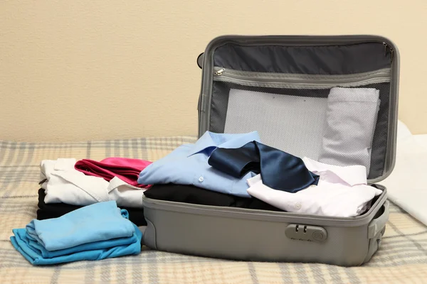 Відкрита сіра валіза з одягом на ліжку — стокове фото