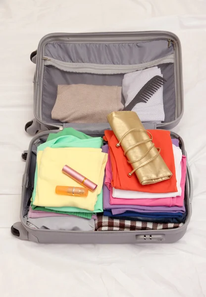 Open grey suitcase with clothing on bed — Stock Photo, Image