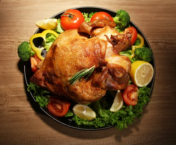 Pollo asado entero con verduras en plato, sobre mesa de madera —  Fotos de Stock